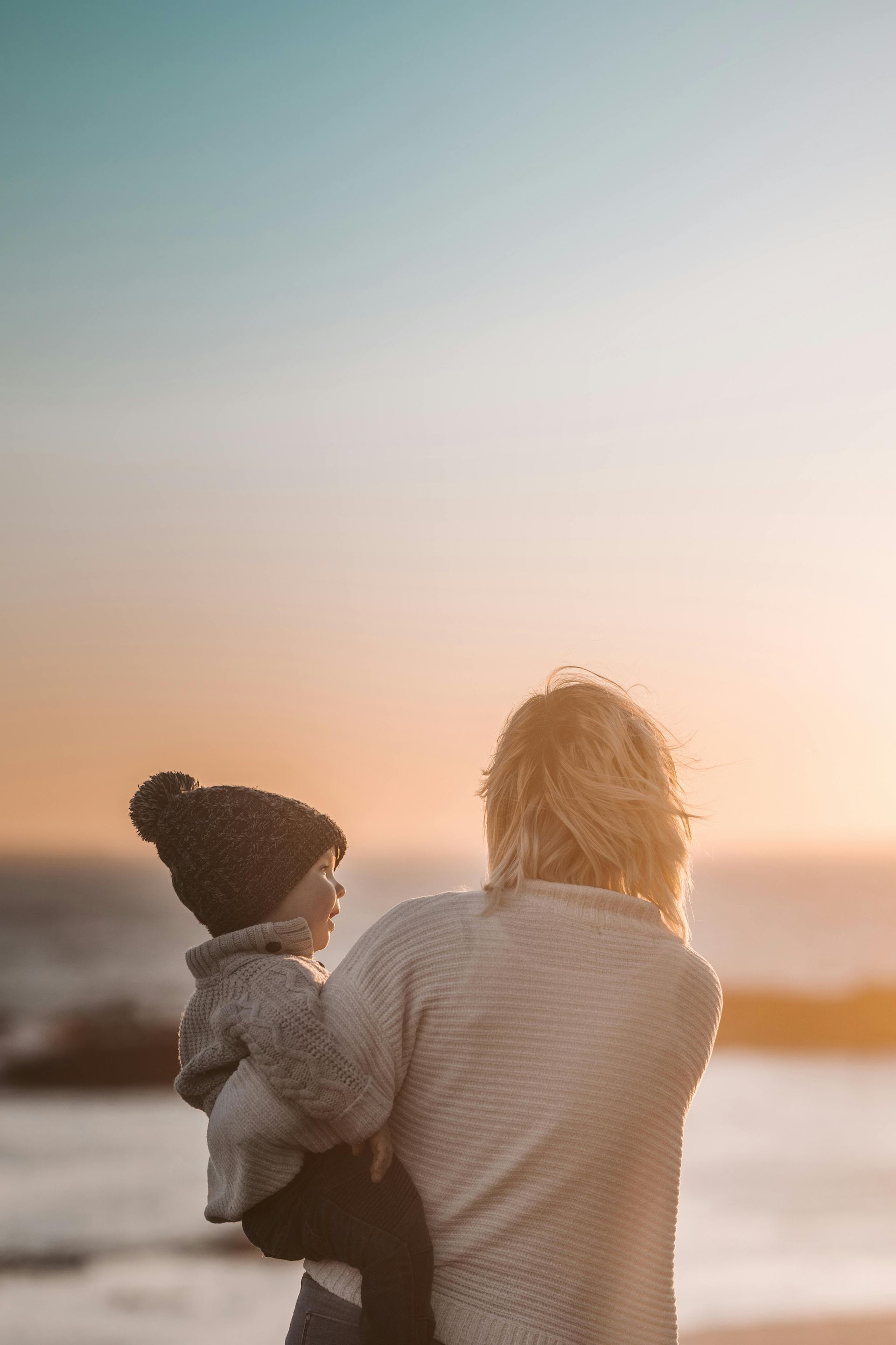 A woman is holding a baby on the beach at sunset.