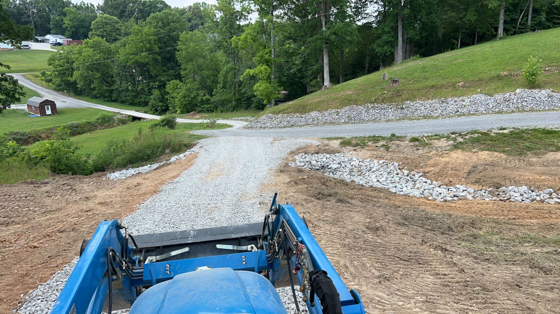 A blue tractor is driving down a gravel road.