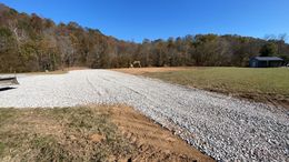 A gravel road going through a field with trees in the background.