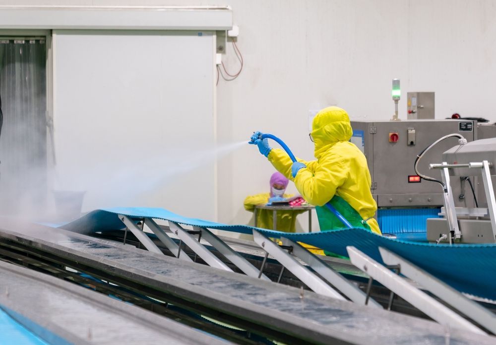 A Man in a Yellow Suit is Spraying Water on a Conveyor Belt in a Factory — Envirokleen Solutions In Slade Point, QLD