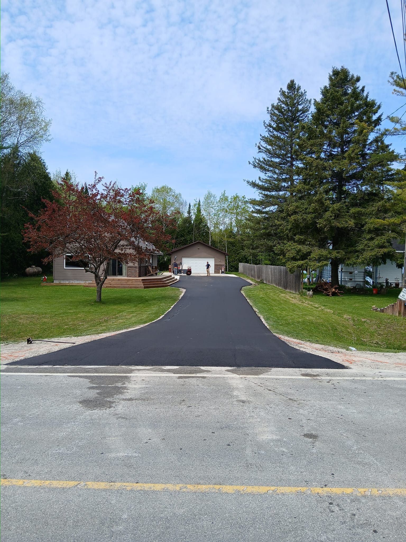 A newly paved driveway leading to a house surrounded by trees.