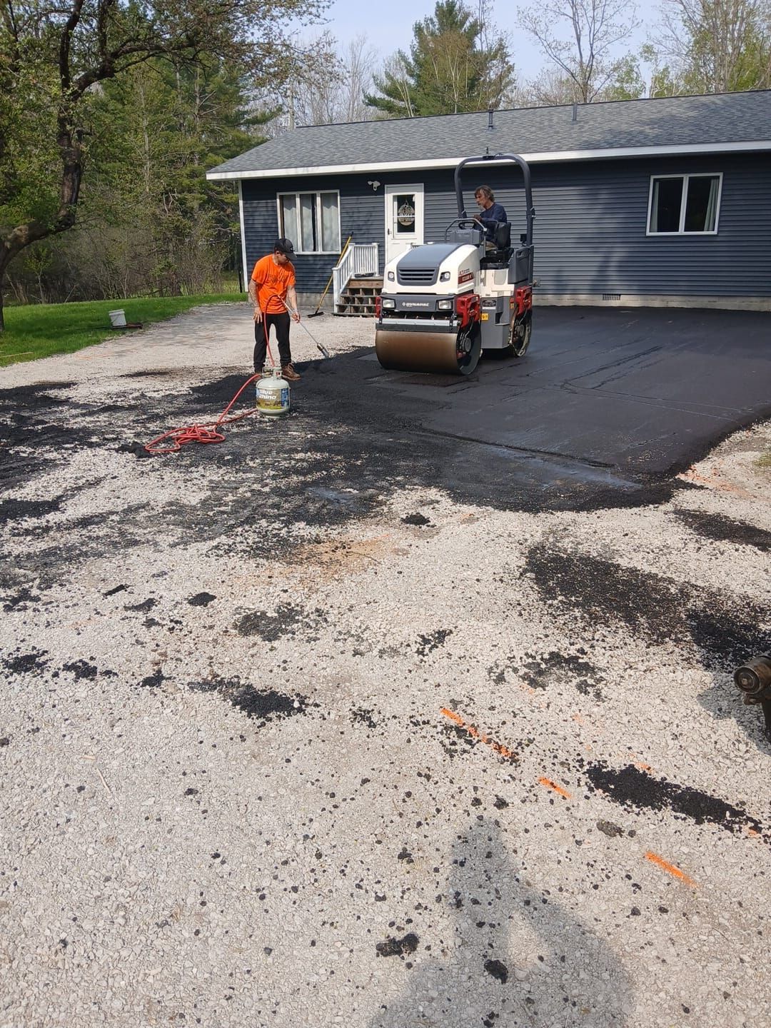 A man is standing next to a roller in a driveway in front of a house.