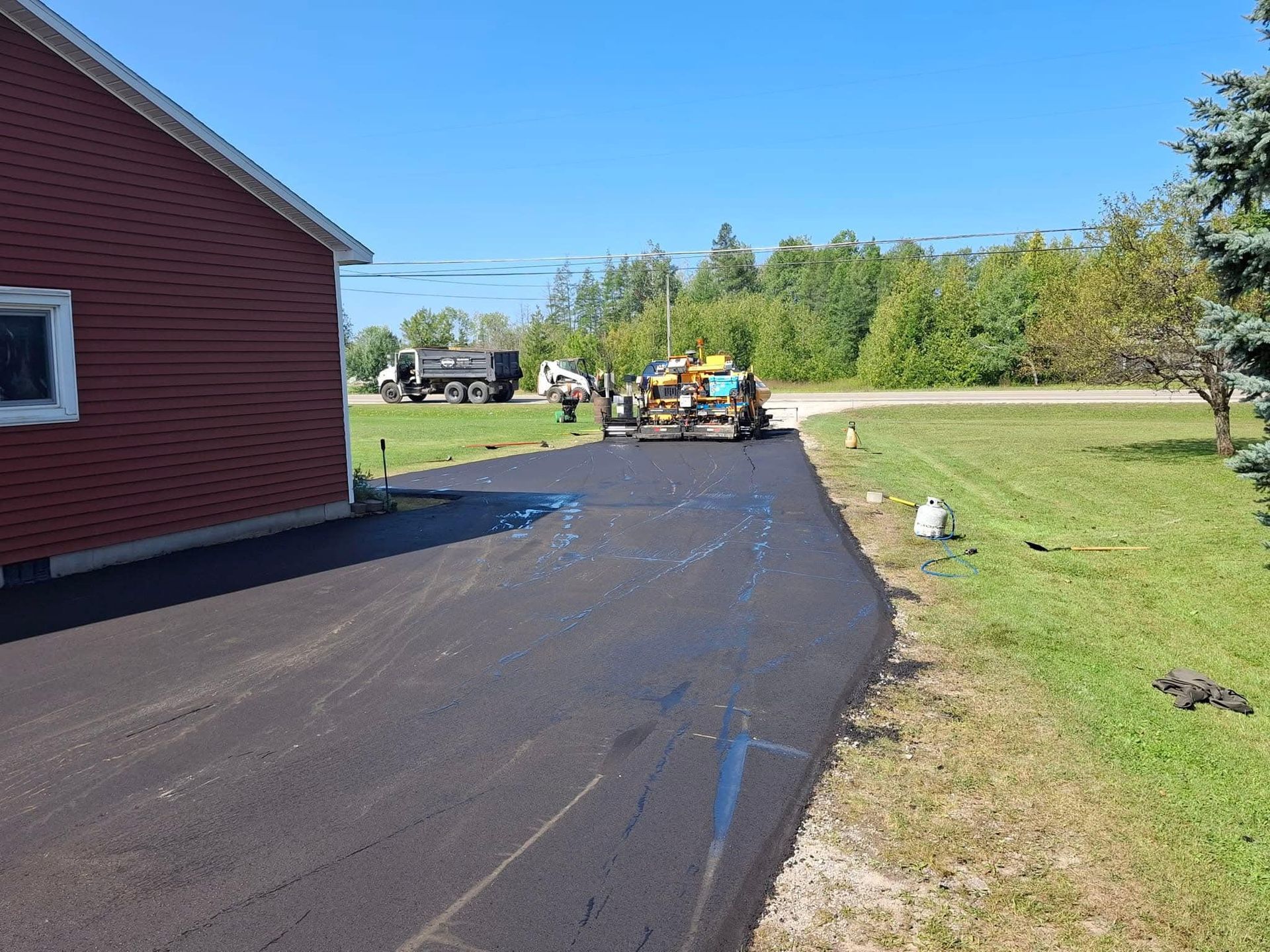 A tractor is driving down a road next to a house.