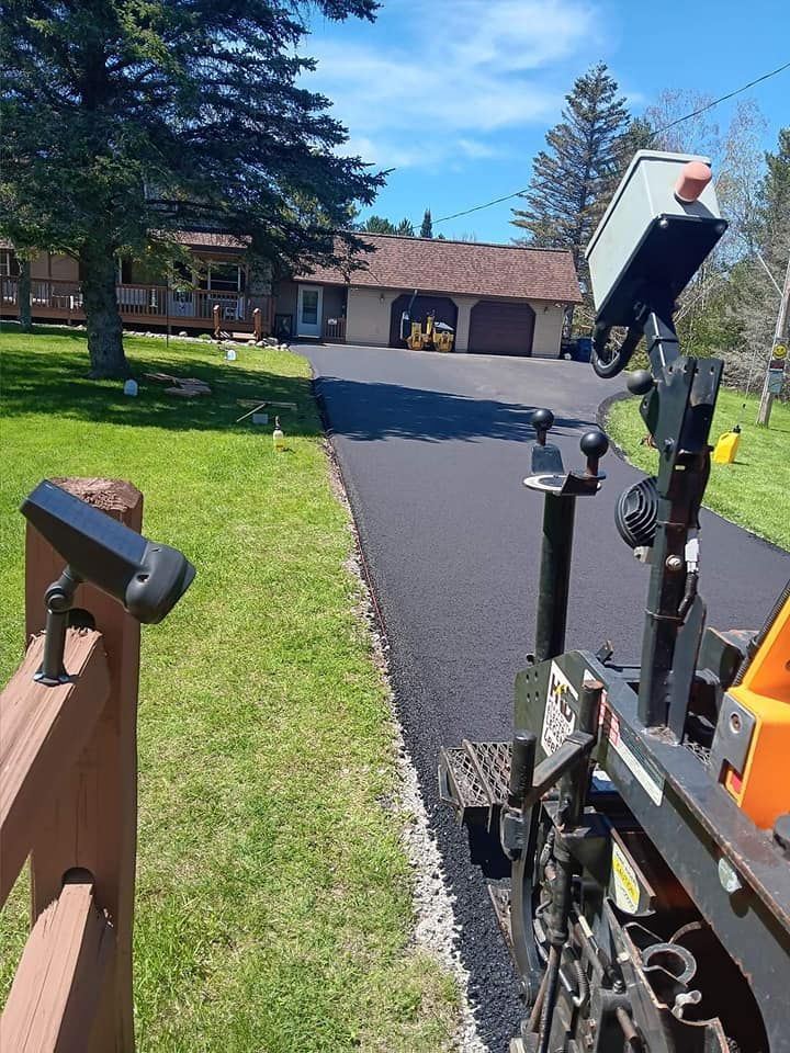A machine is laying asphalt on a driveway in front of a house.