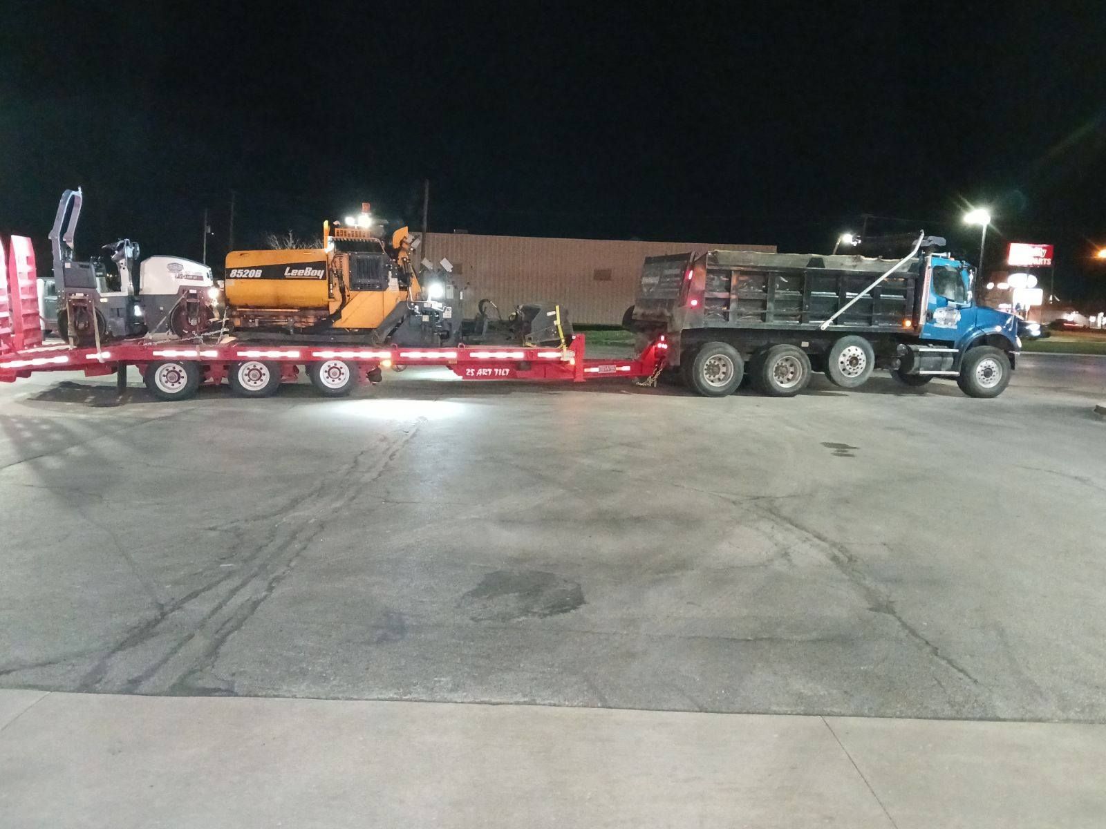 A semi truck is towing a dump truck in a parking lot at night.