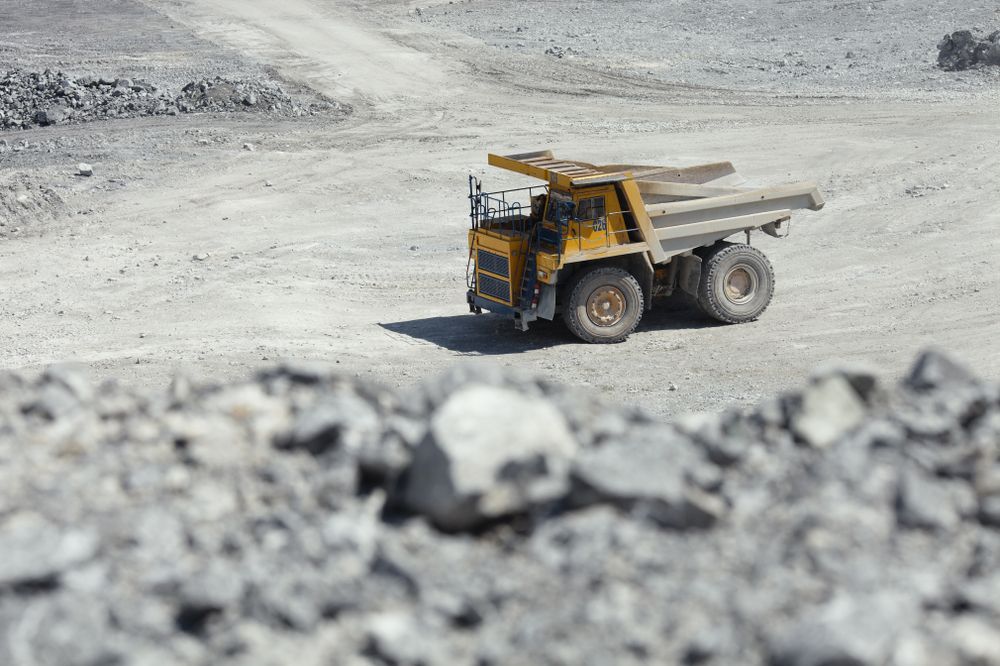 A Yellow Dump Truck is Driving Down a Dirt Road in a Quarry — PBC Compliancing Pty Ltd in Mackay, QLD
