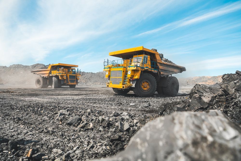 Two Dump Trucks Are Driving Down a Dirt Road in A Coal Mine — PBC Compliancing Pty Ltd in Paget, QLD