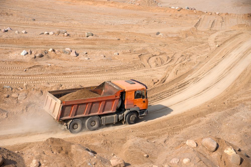 Orange Dump Truck Is Driving Down a Dirt Road — PBC Compliancing Pty Ltd in Moranbah, QLD