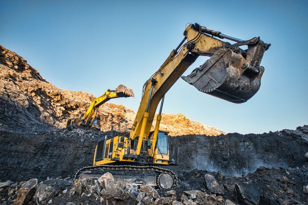 Yellow Excavator Digging Into a Pile of Dirt Against a Blue Sky — PBC Compliancing in Whitsundays, QLD