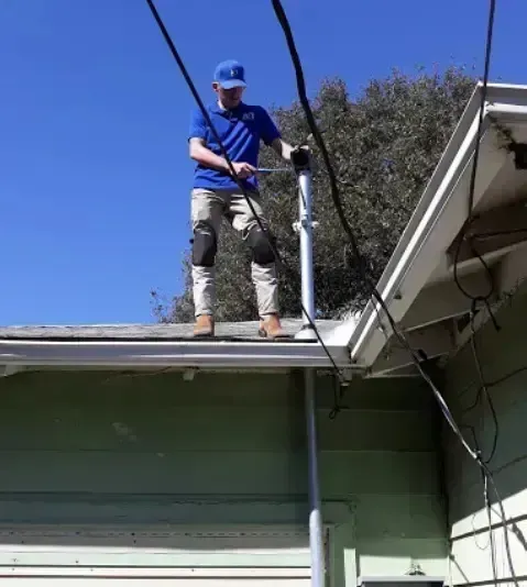 Local Electricians – Local electricians are seen working on the roof of a residential home, performing essential maintenance or repairs on the electrical conduit and service connection.