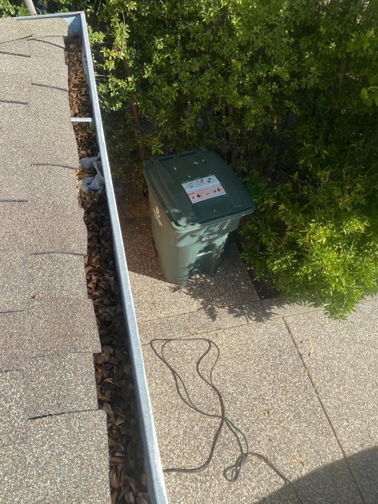 A green trash can is sitting next to a gutter on a sidewalk.