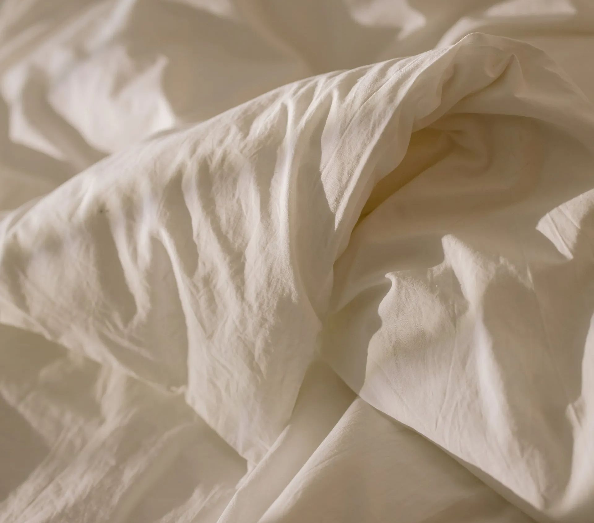 A close up of a white blanket on a bed.