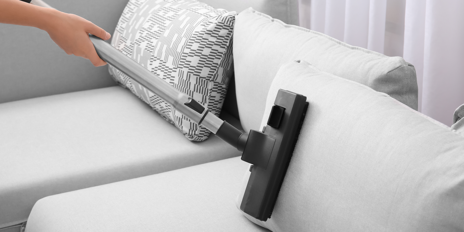 A person is cleaning a couch with a vacuum cleaner.