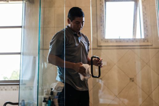 A man is cleaning a shower door in a bathroom.