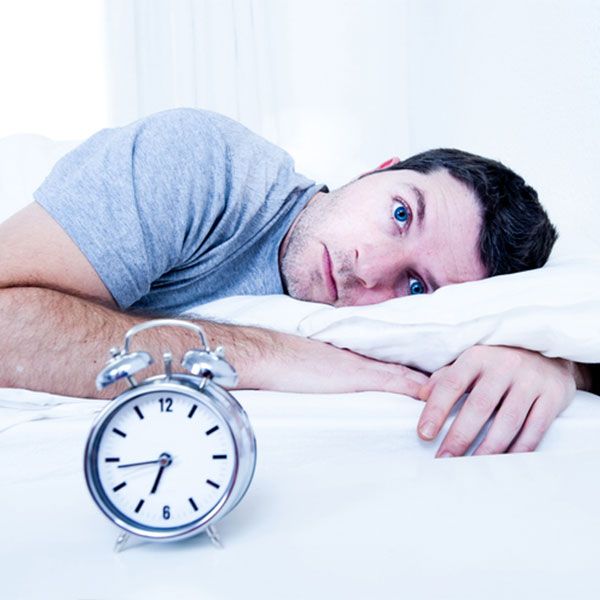 Man with insomnia lying awake in bed with alarm clock