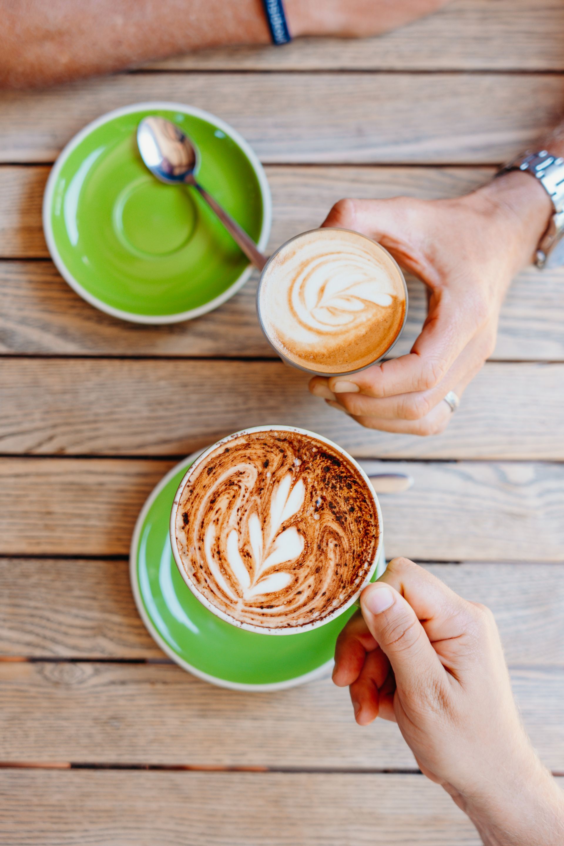 Two people are holding cups of coffee on a wooden table.