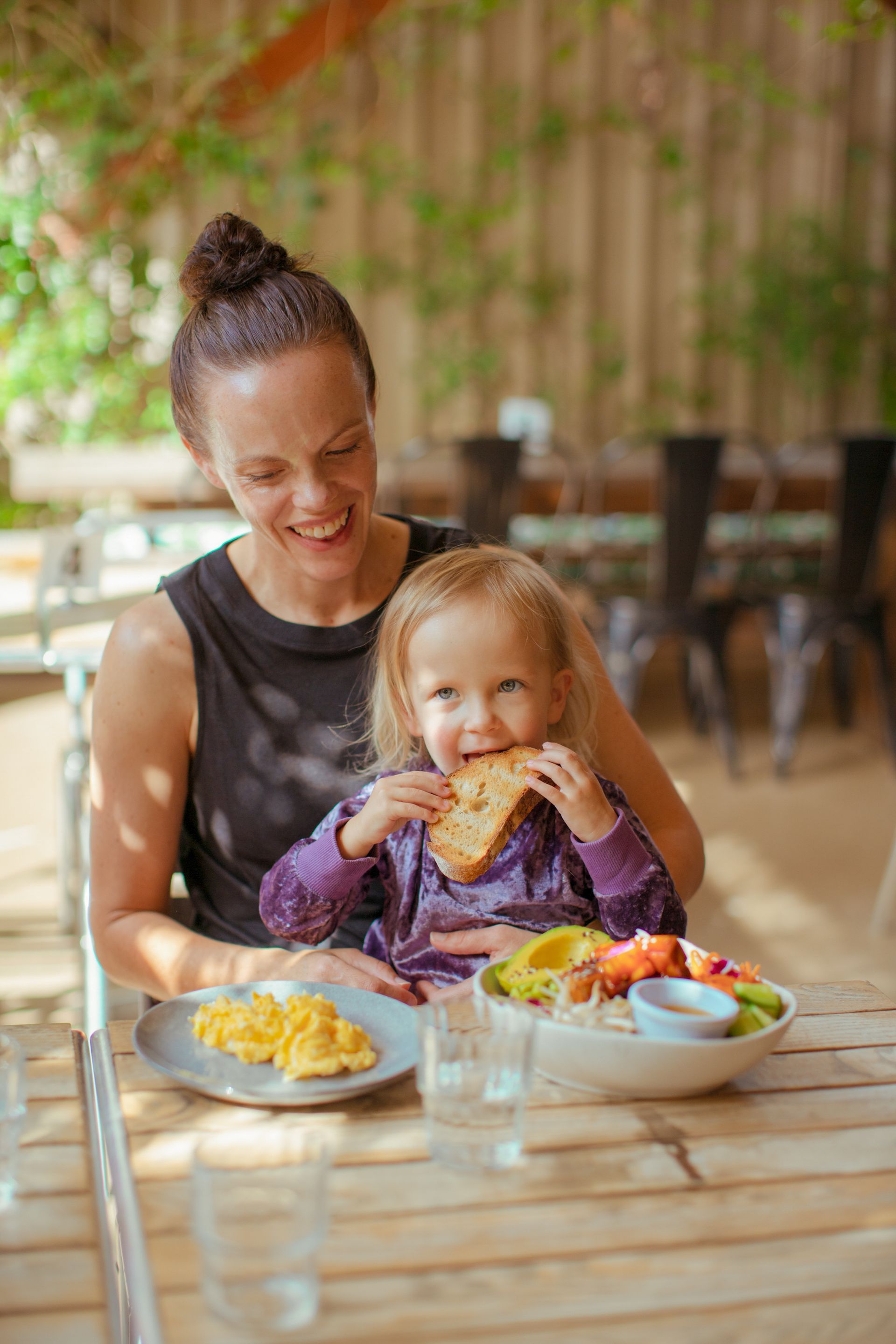 A woman and a little girl are sitting at a table eating food.