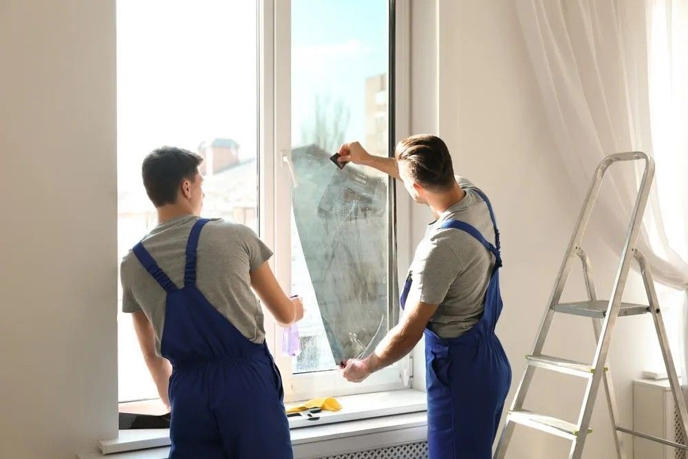 Two Men Are Installing Window Film on A Window in A Room — Solarmaster in Gold Coast, QLD