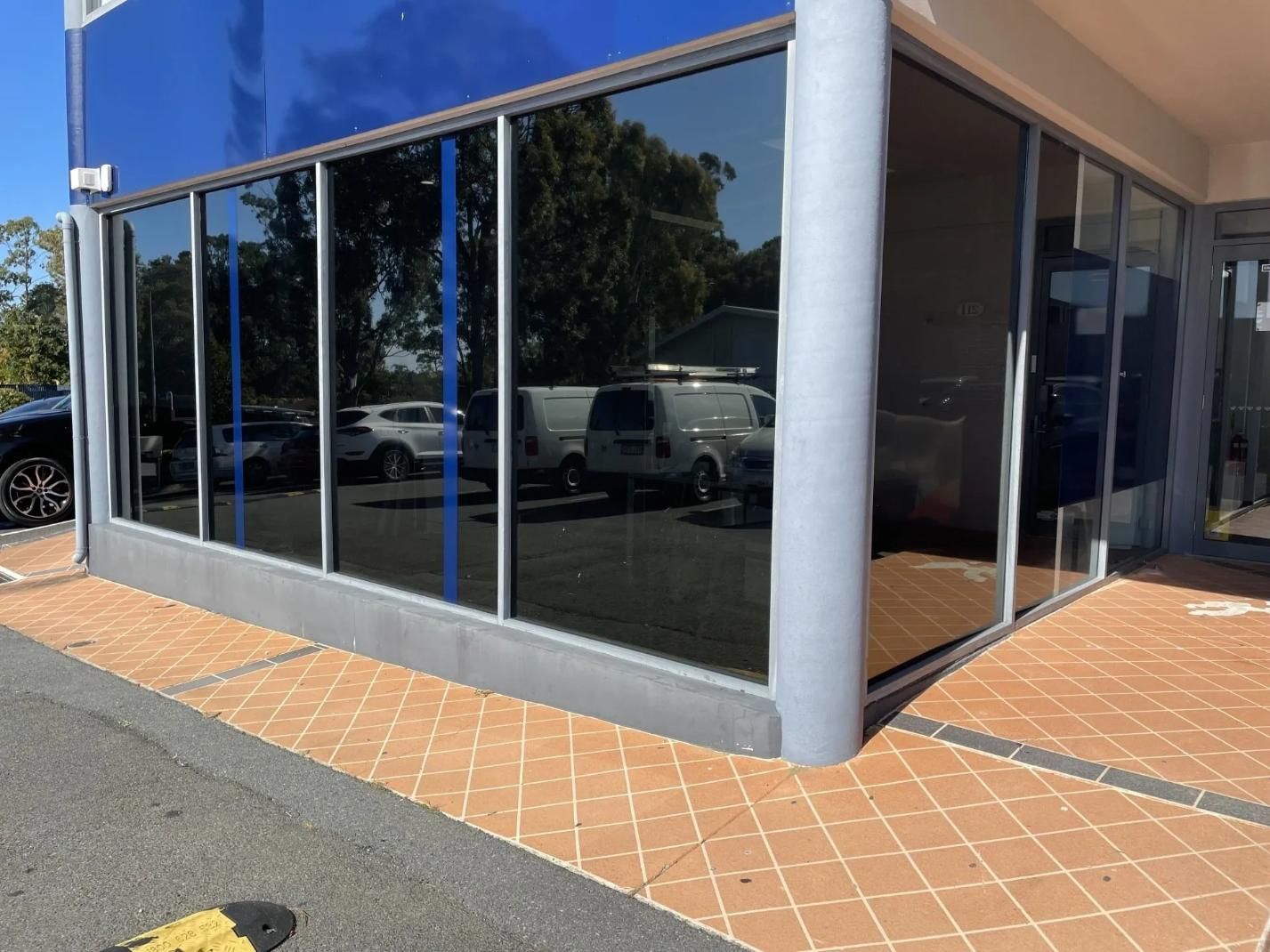 Building With Tinted Windows Reflecting Vehicles In A Parking Lot, Next To A Paved Area