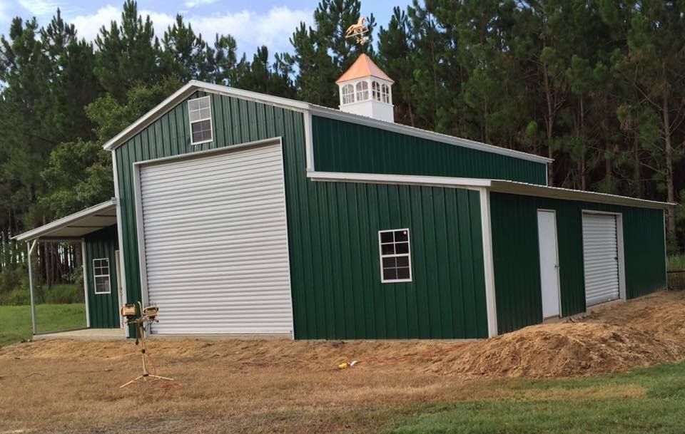 Green metal barn with white garage door, small windows, and a cupola.