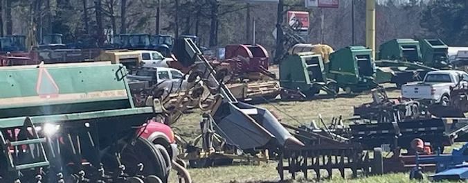 Agricultural equipment at a farm equipment auction. Several tractors, balers, and tillers are displayed outdoors.