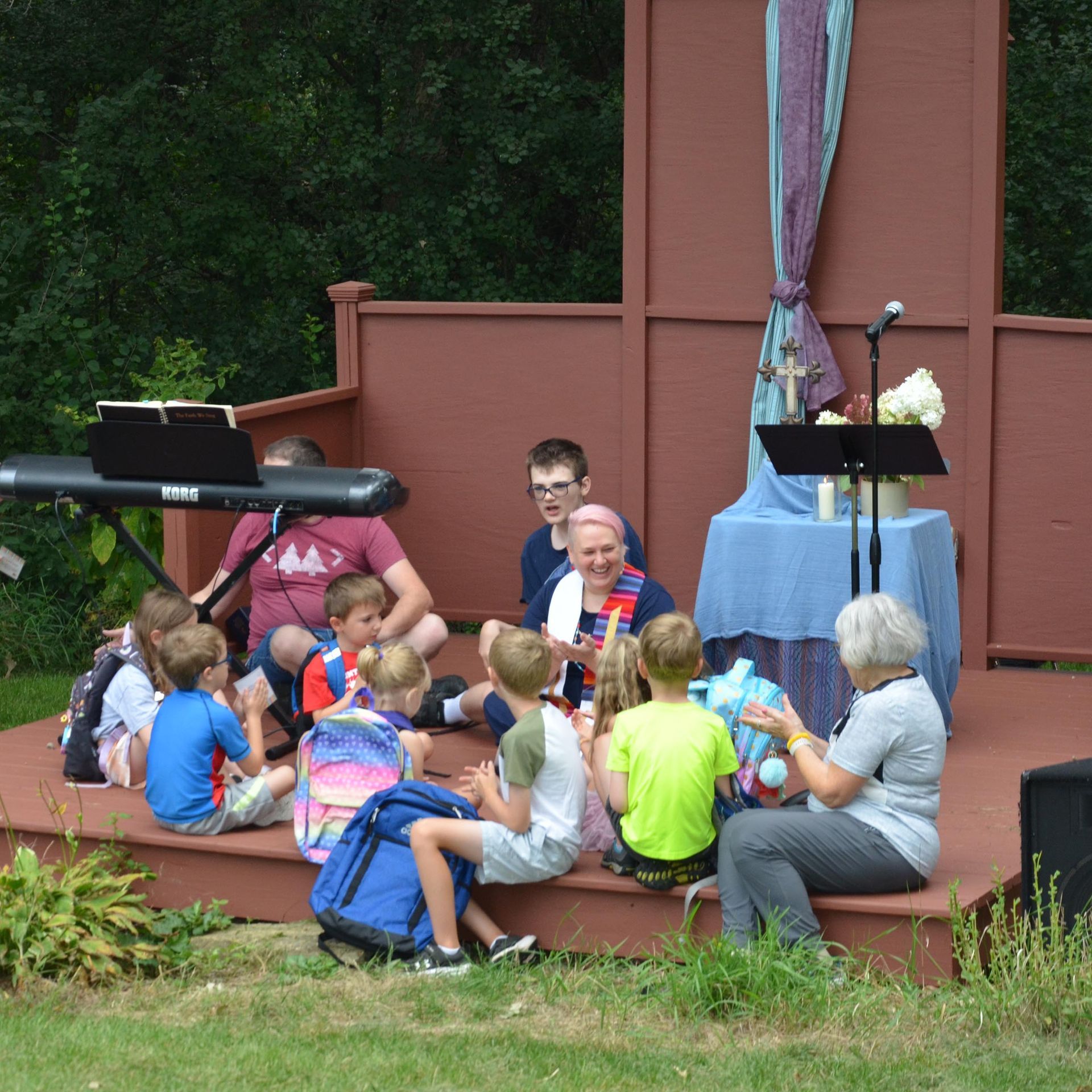 Children and adults gathered outdoors on a wooden stage, likely for a community event.