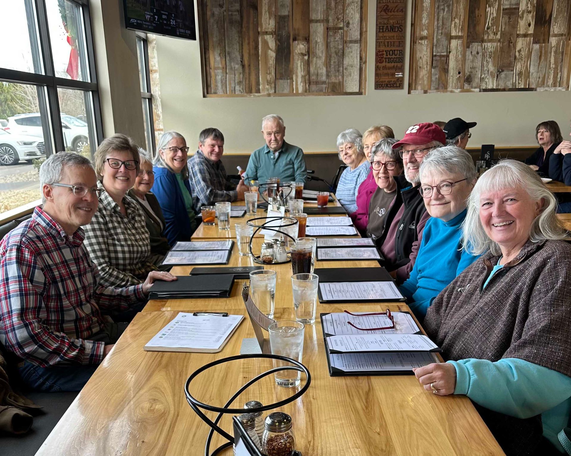 People eating at a wooden table, plates of food, bread, and bowls of salads are in the center.