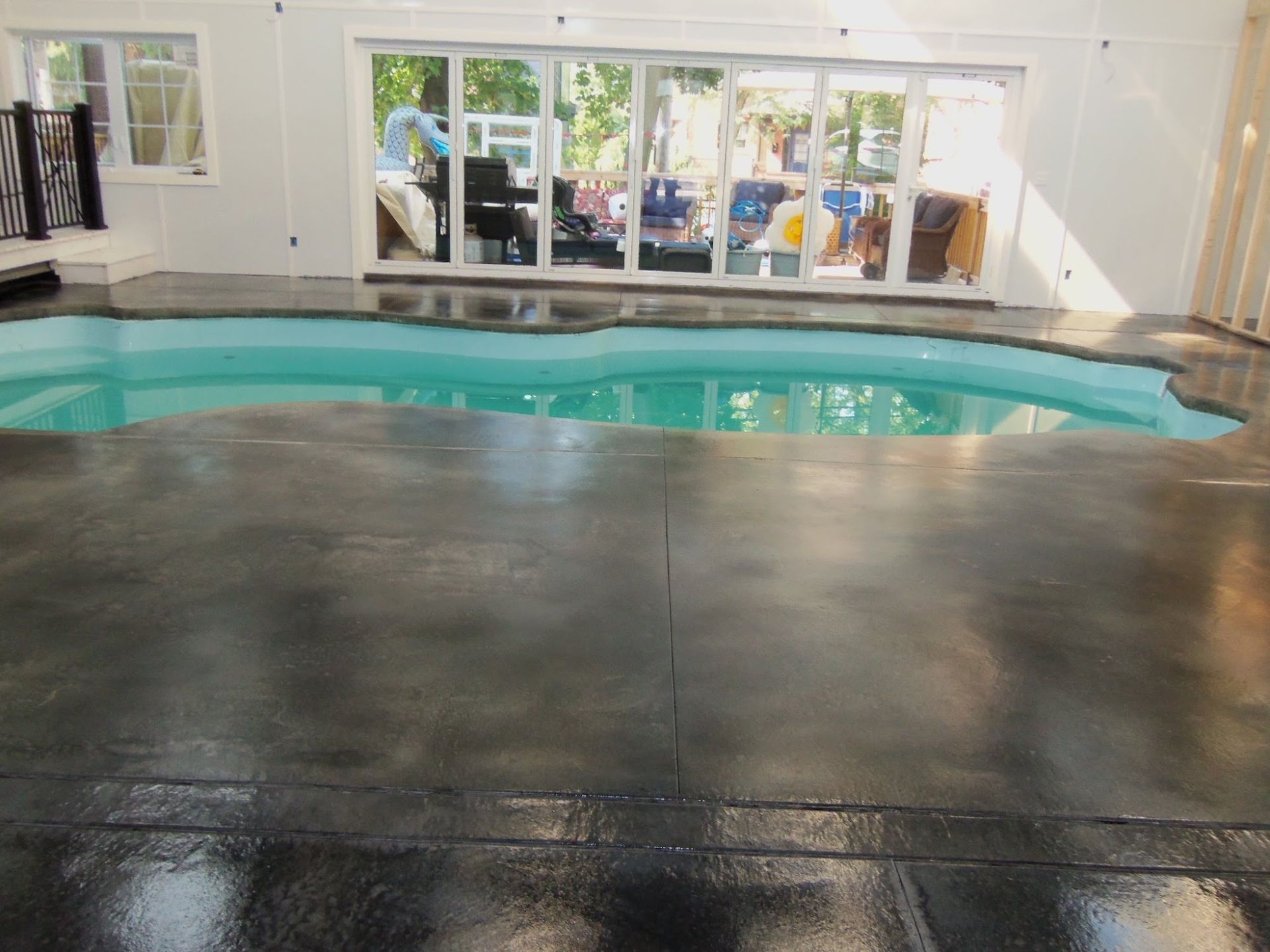 Indoor pool with gray concrete flooring and glass doors, reflecting sunlight and people.