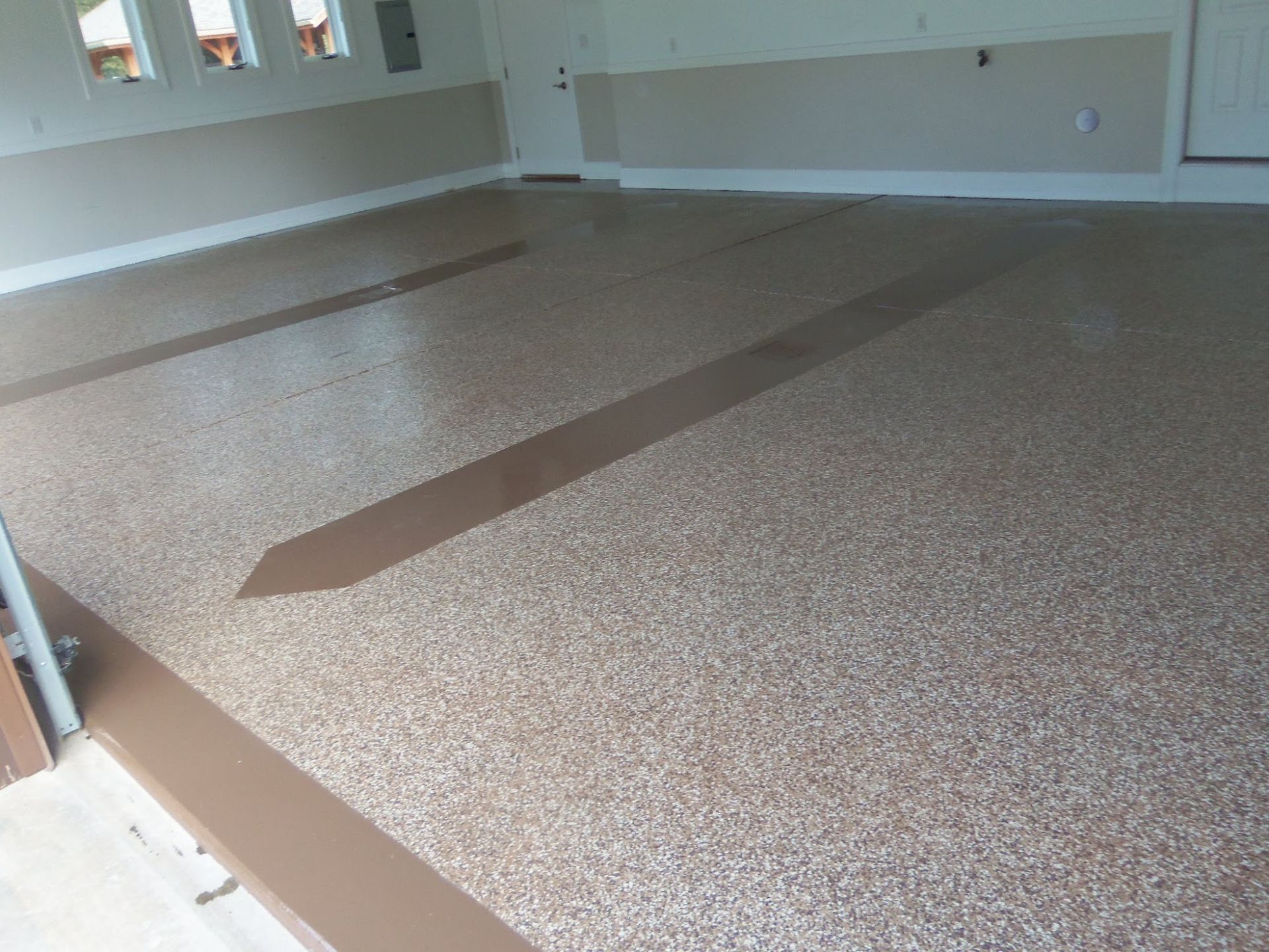 Garage with speckled epoxy floor, brown borders, and accent stripes. Beige and brown tones dominate.