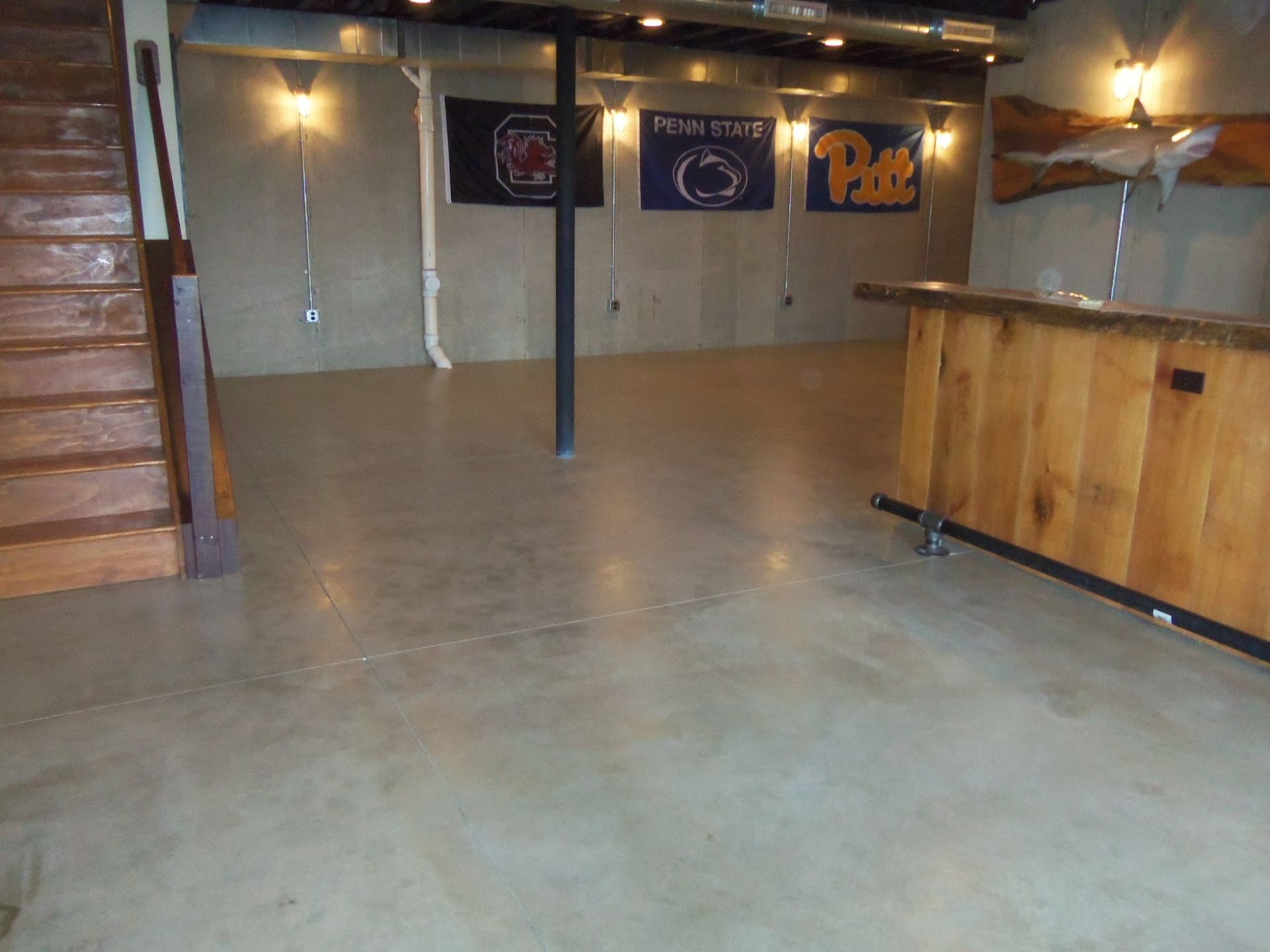 Basement entertainment area with a bar, flags, and a wooden staircase. Concrete floor.