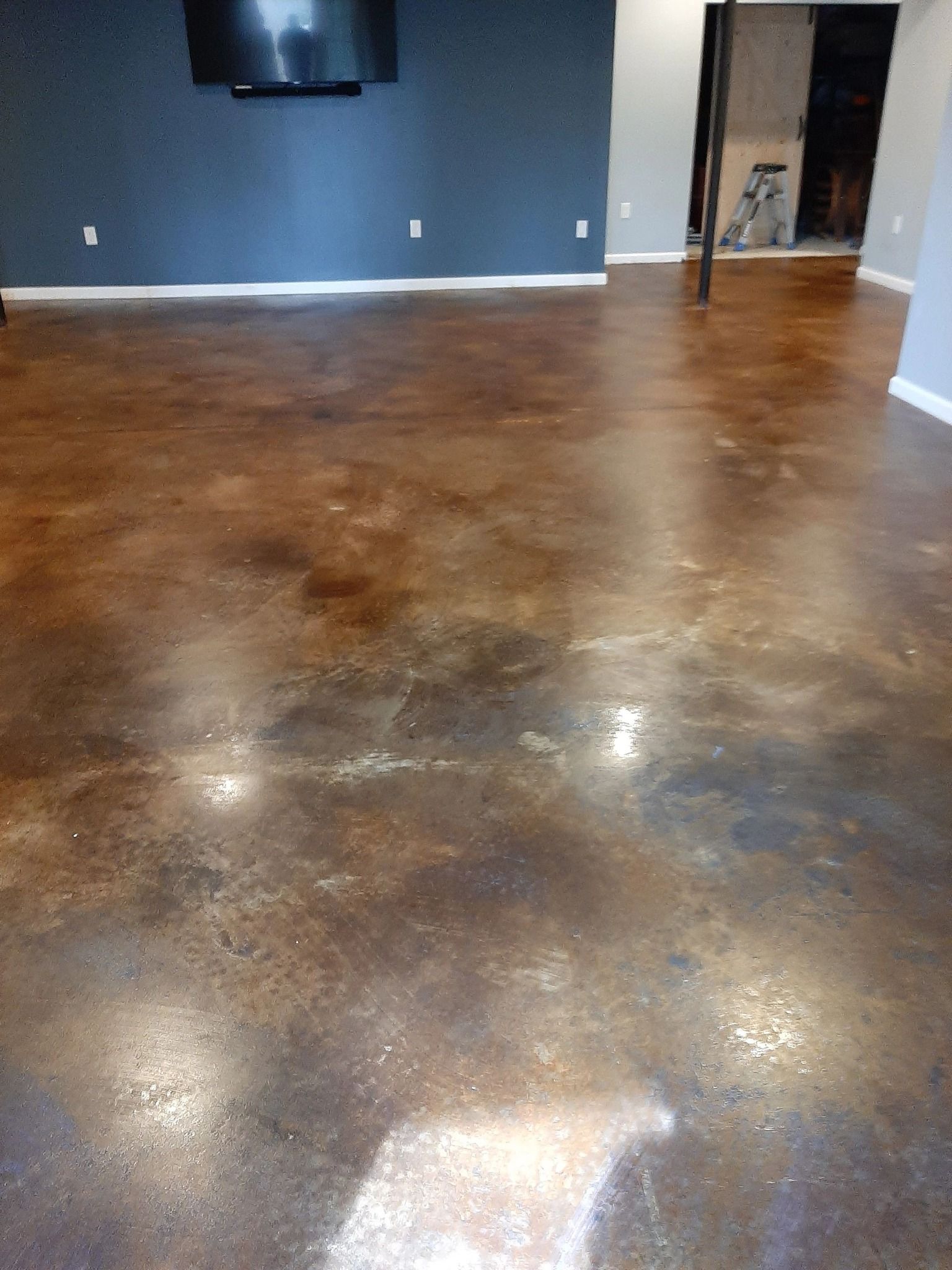 Brown and bronze stained concrete floor in a room with dark blue wall and TV.