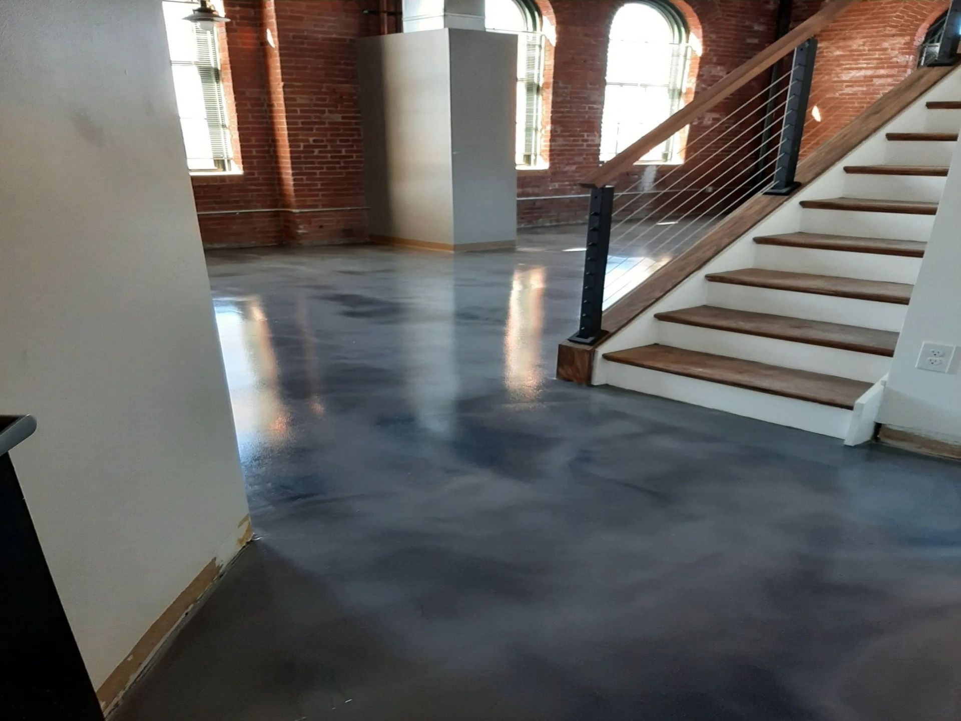 Open-concept space with a concrete floor, exposed brick walls, and a wooden staircase with a cable railing.