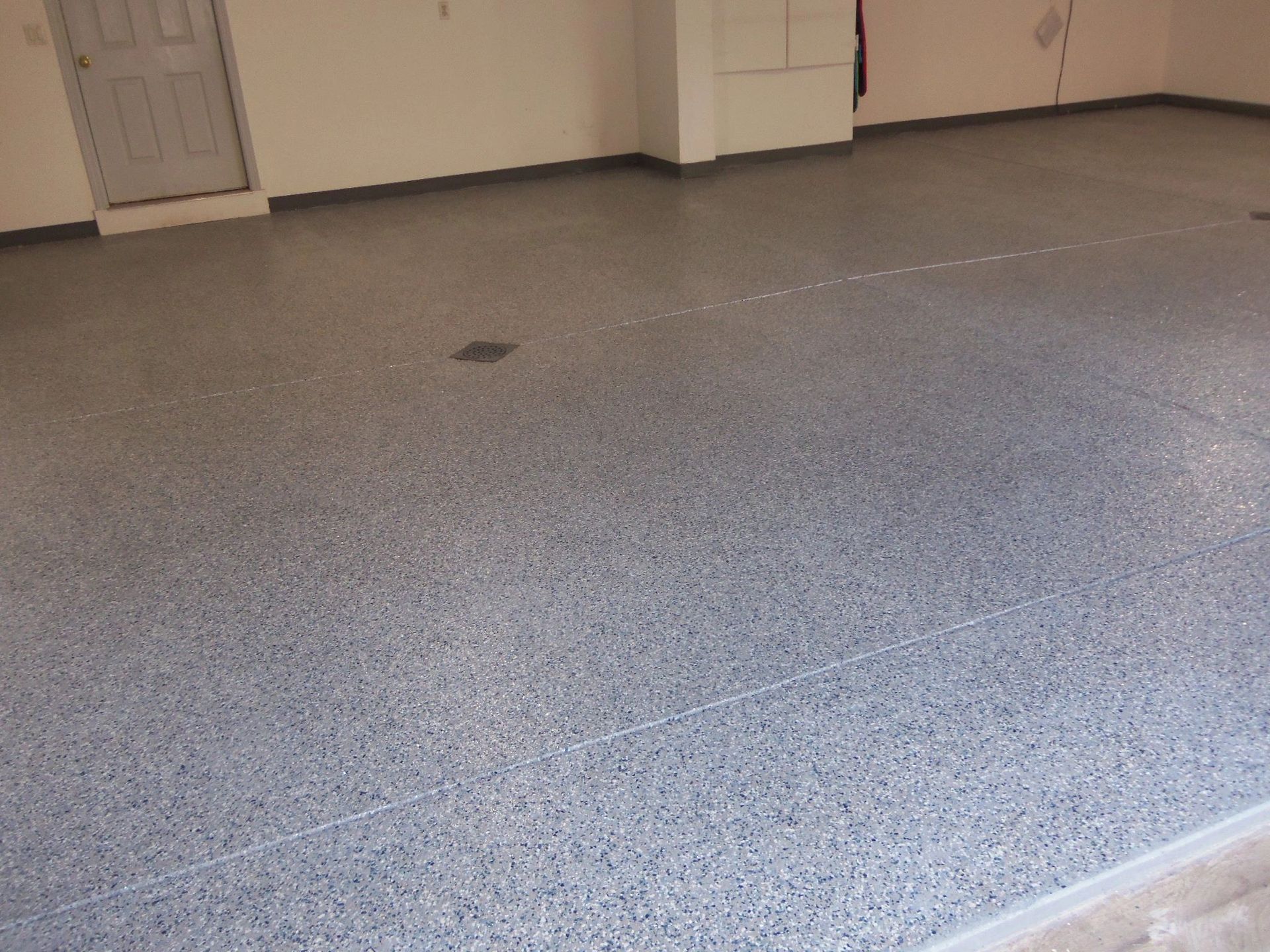 Gray speckled epoxy floor in a garage with a door and white walls.