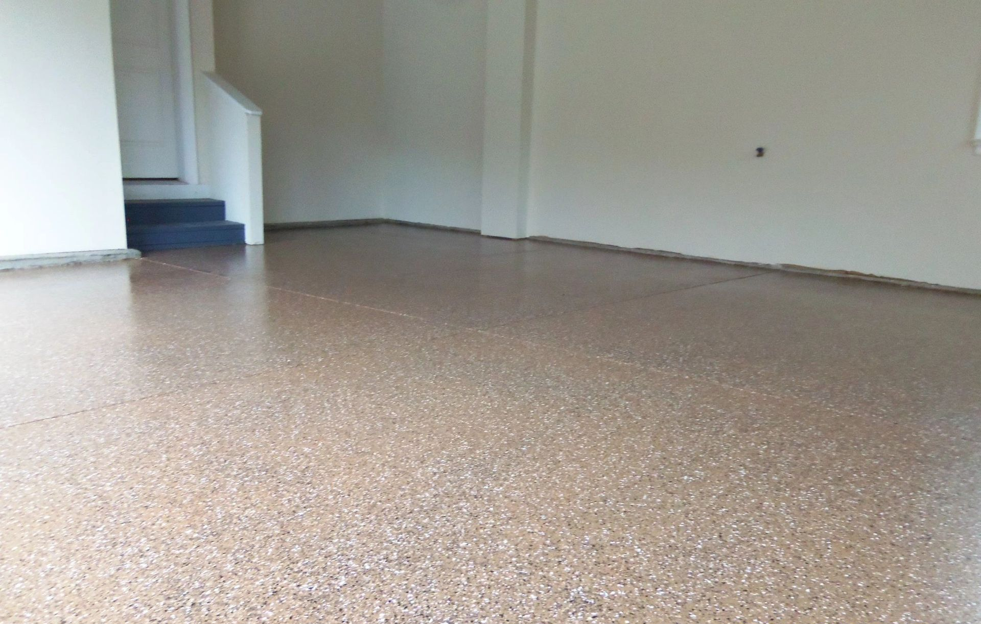 Garage interior with a speckled epoxy floor, white walls, and a stairway in the background.