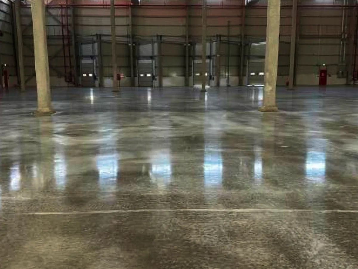 Polished concrete warehouse floor reflecting overhead lights and doorways.