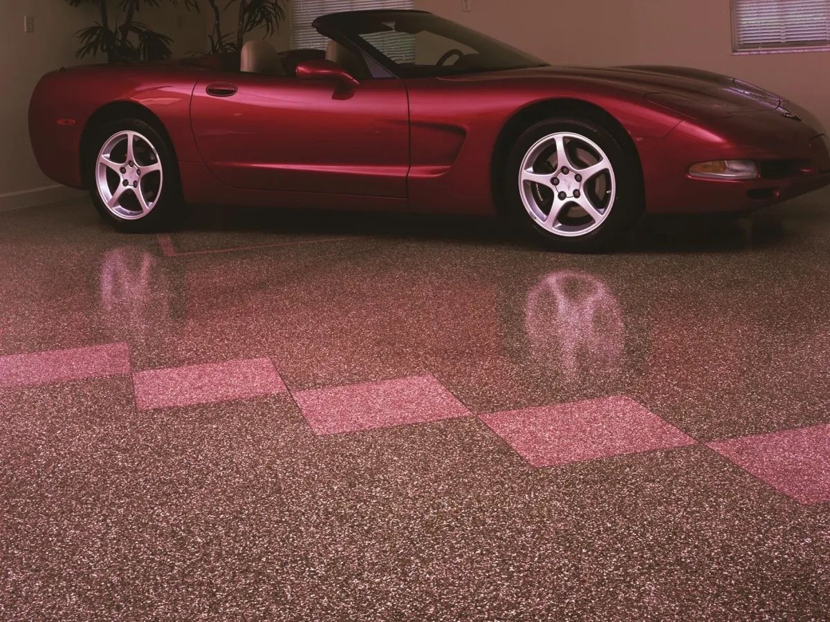 Red Corvette parked on a decorative, speckled garage floor with checkerboard pattern.