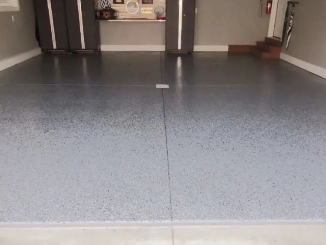 Garage with speckled gray epoxy floor. Garage door and storage cabinets in background.