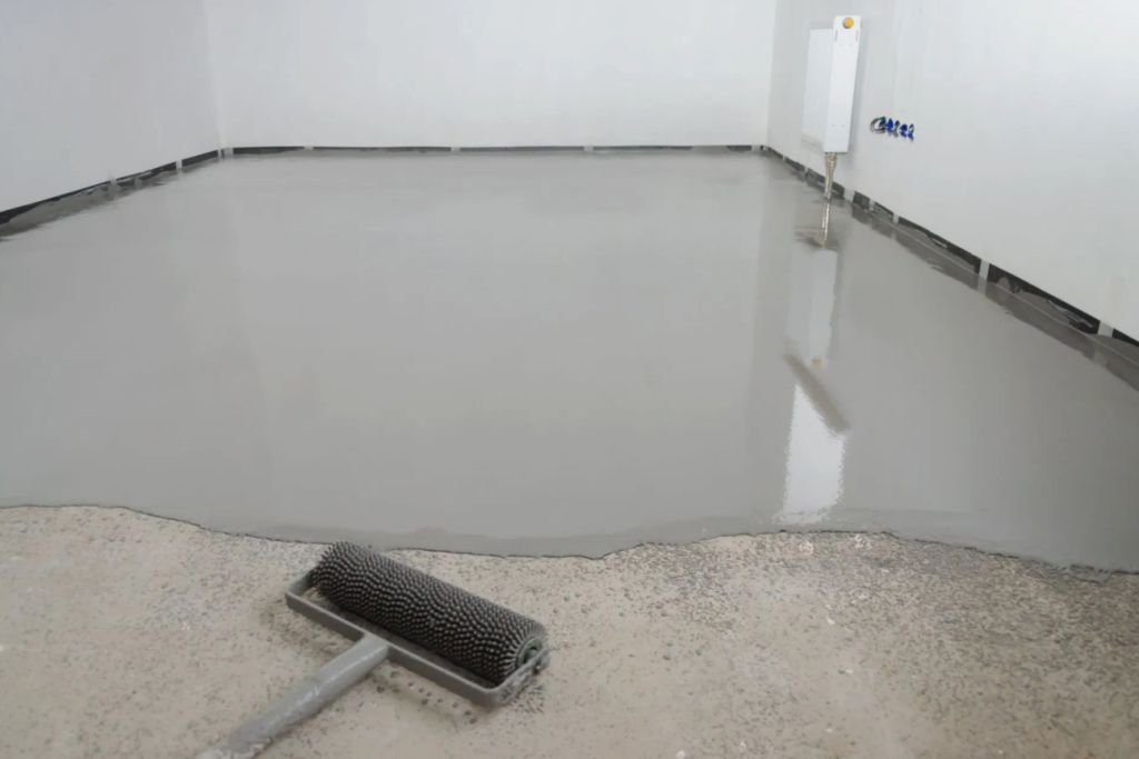 Gray, epoxy-coated floor in a room, with a roller and bucket visible.