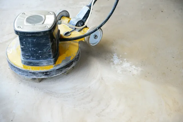 Yellow and black floor grinder polishing a concrete surface, creating dust.