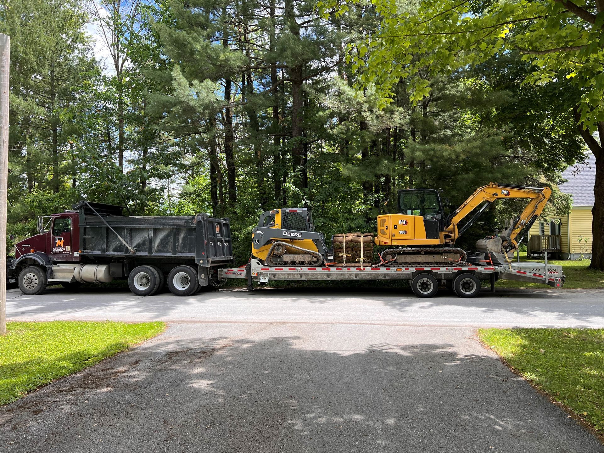 Un gros camion à benne basculante tractant une remorque à plateau transportant deux pièces d'équipement de construction jaune.
