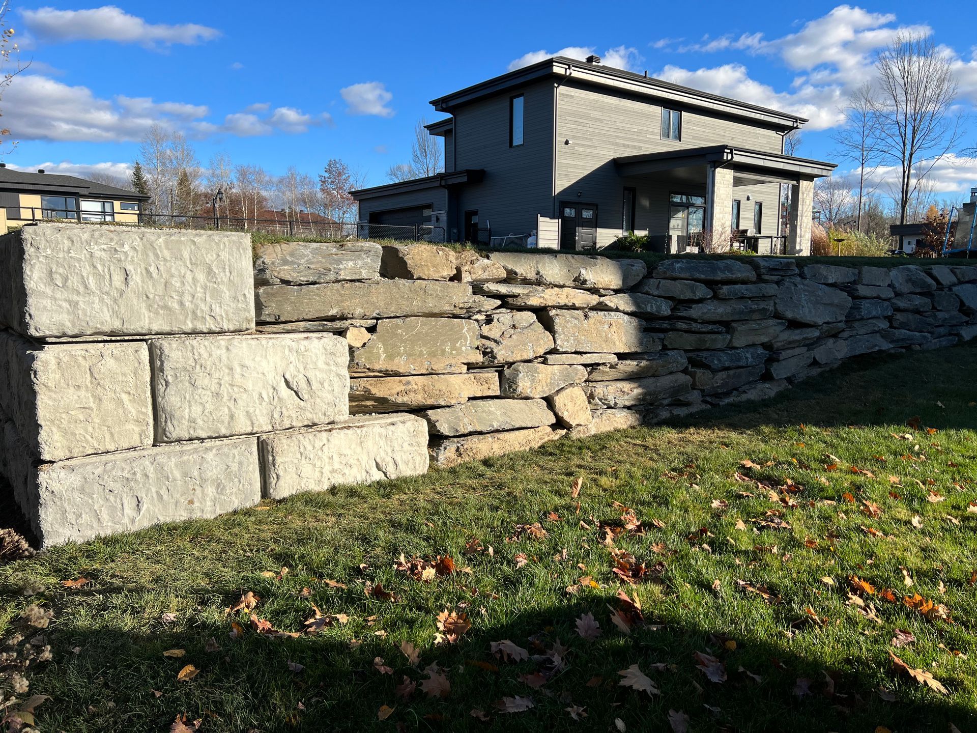 Un grand mur de pierre se trouve au milieu d'un champ verdoyant devant une maison.