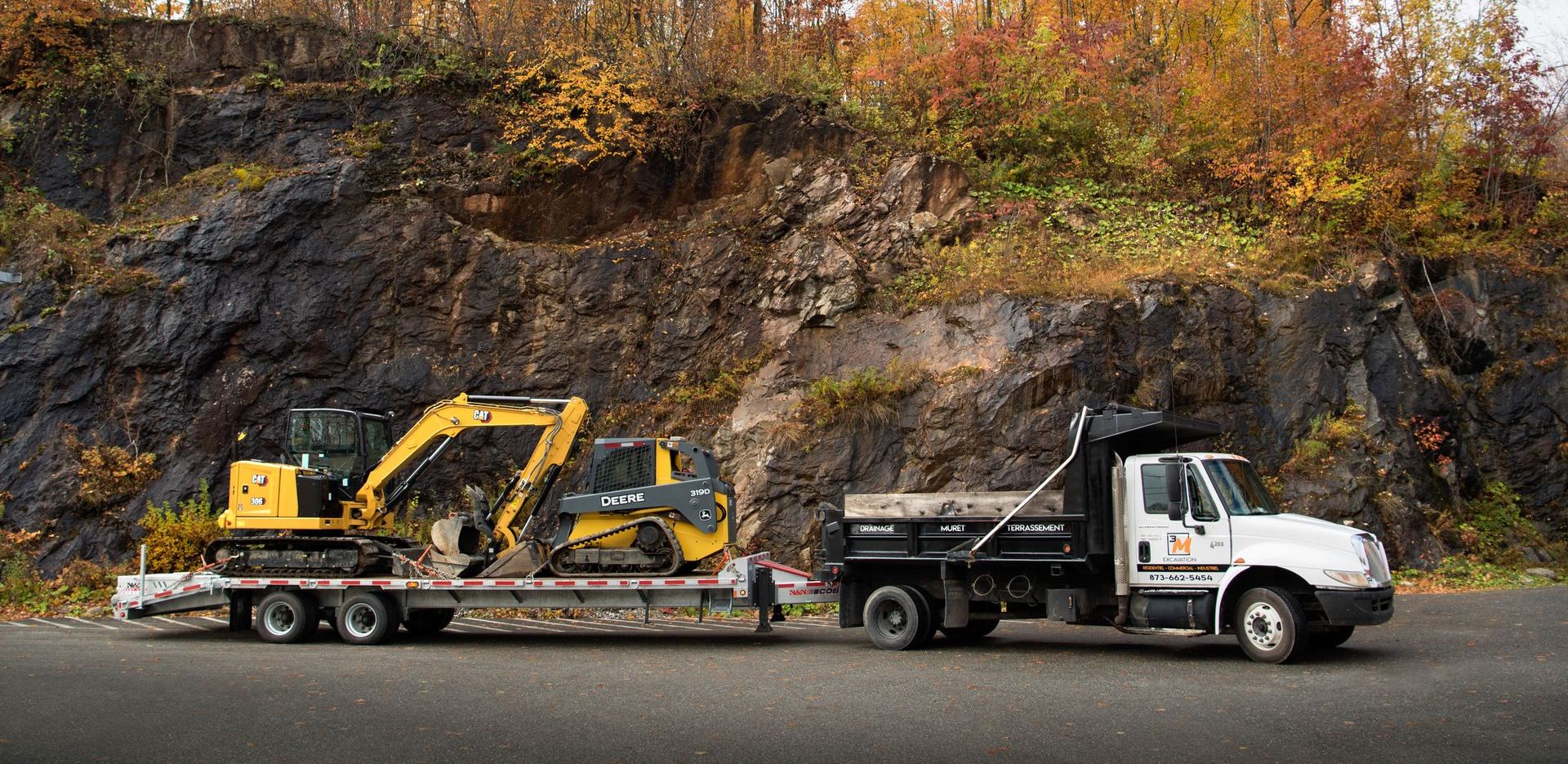 Un camion blanc remorque une excavatrice jaune sur une remorque à plateau.