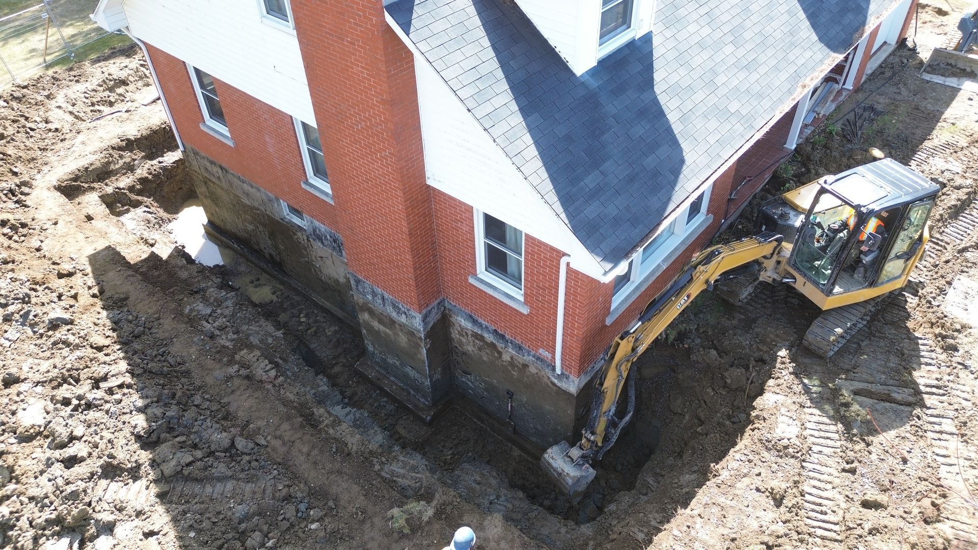 Excavatrice creusant autour des fondations d'une maison en briques ; terre, construction.