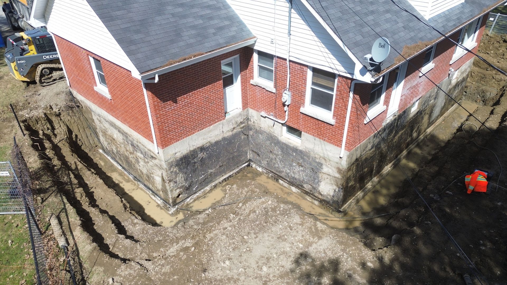 Extérieur d'un bâtiment en briques rouges aux fondations apparentes. Un ouvrier en gilet orange à droite.