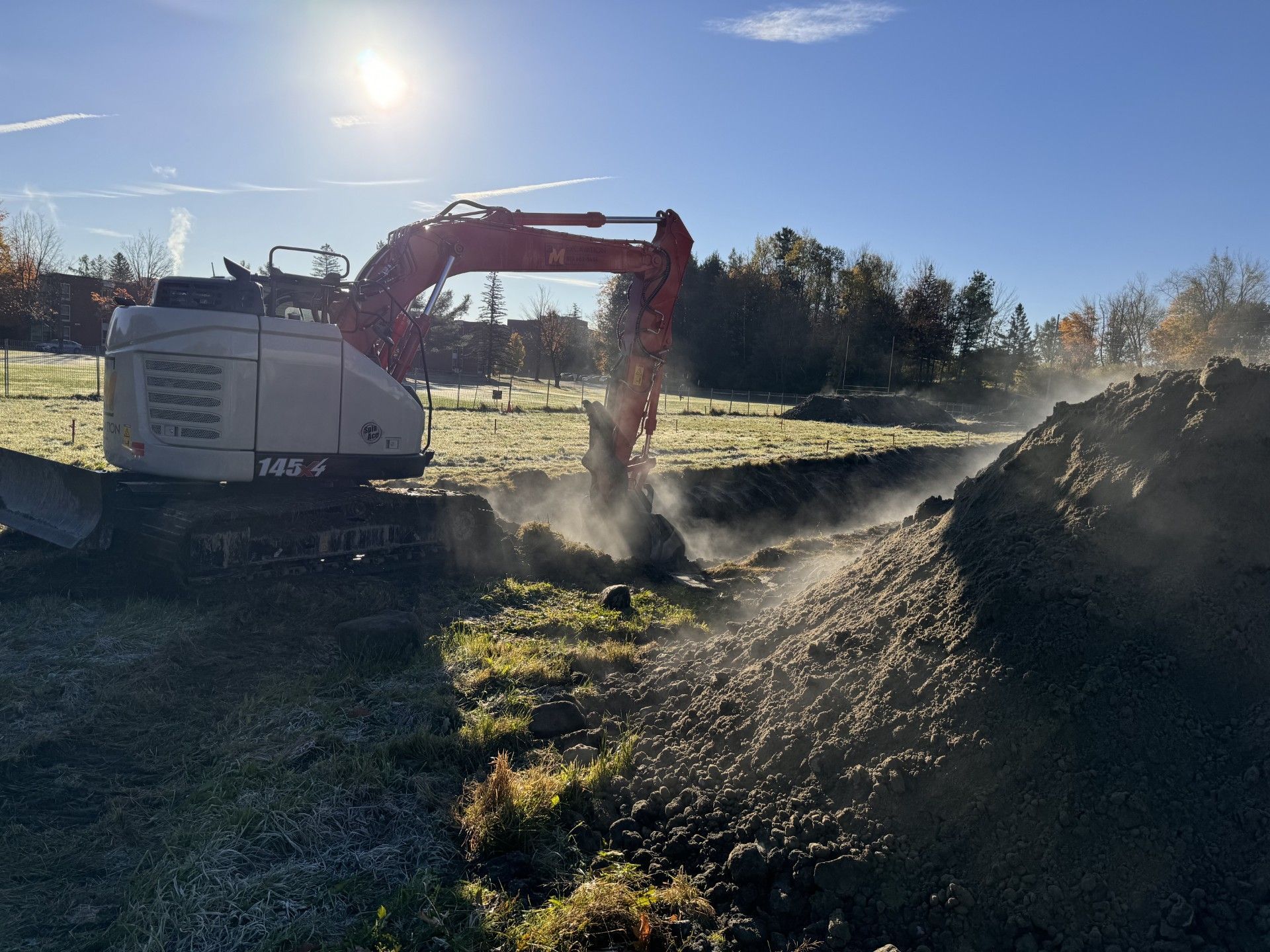 Une excavatrice creuse dans un champ sous un soleil éclatant, soulevant de la terre.