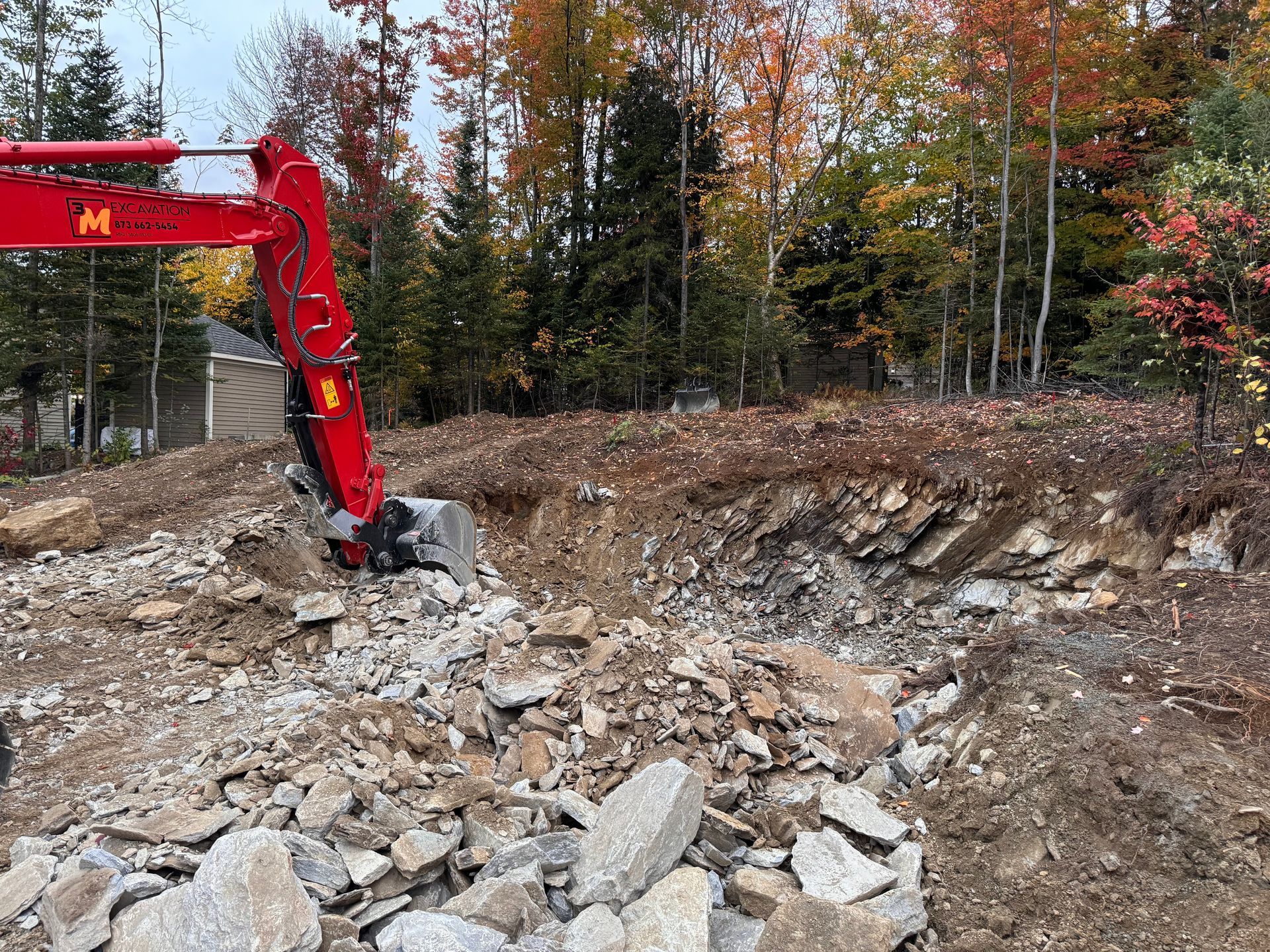 Excavatrice rouge creusant dans un sol rocheux près du feuillage d'automne.