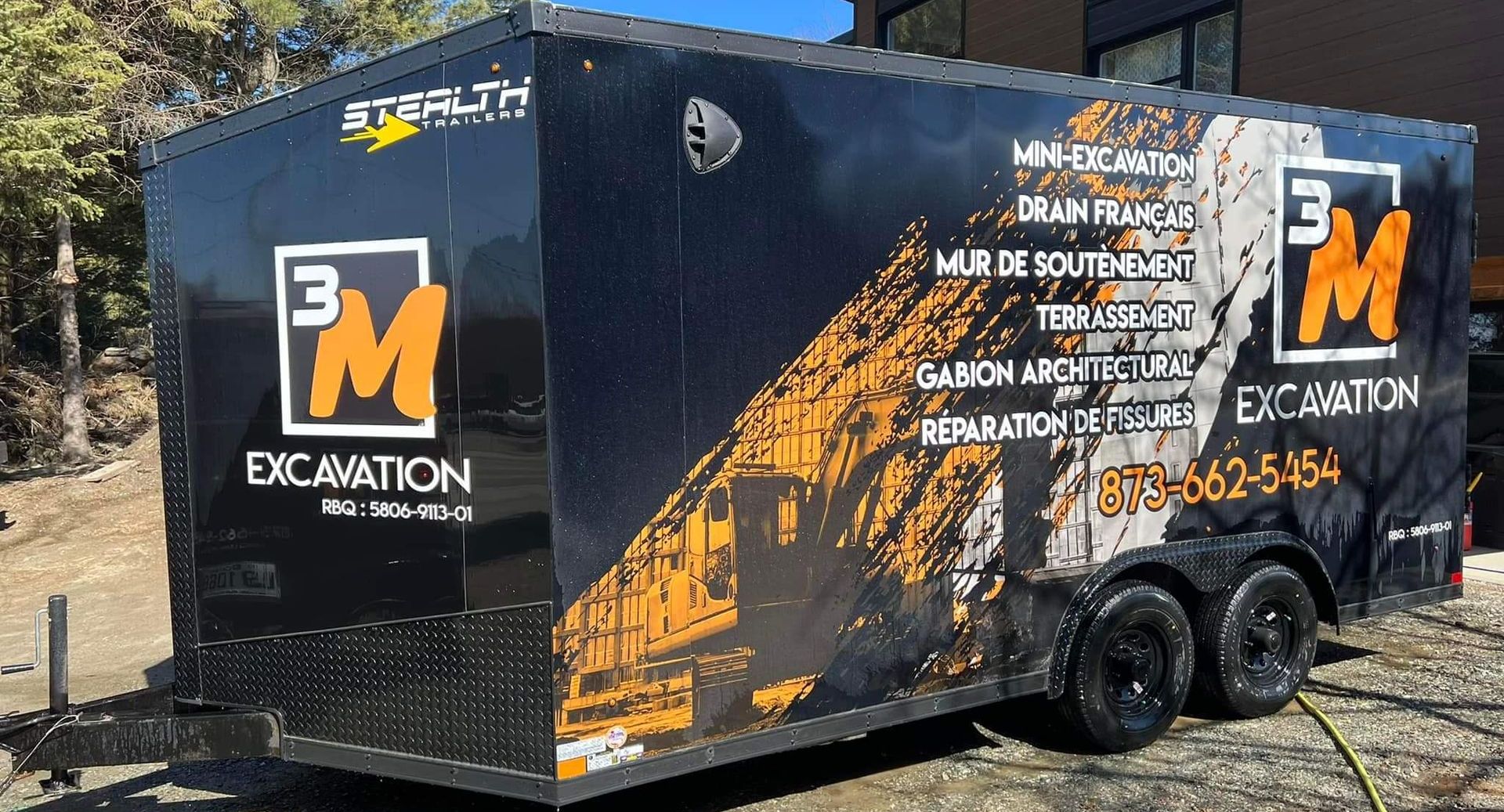 Une remorque noire avec le mot excavation dessus est garée sur un parking.