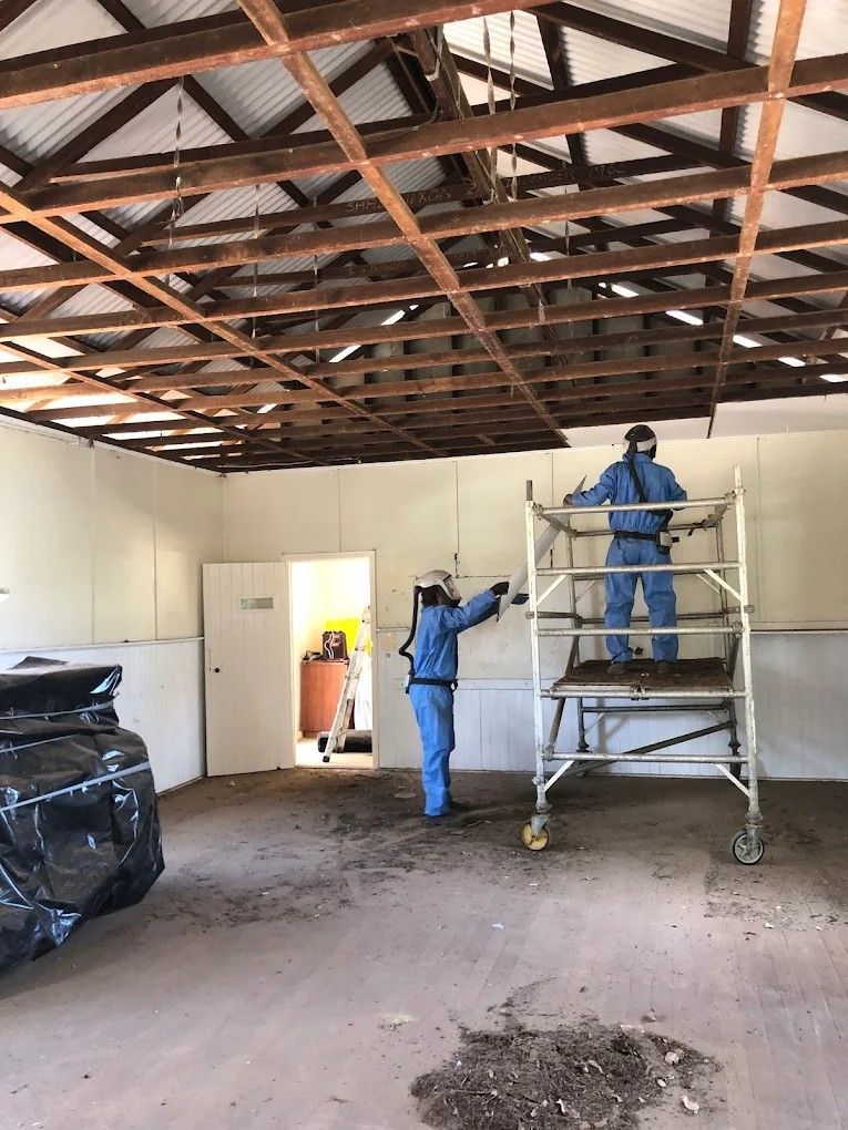 Worker in white protective gear installing a black roofing membrane on a flat roof