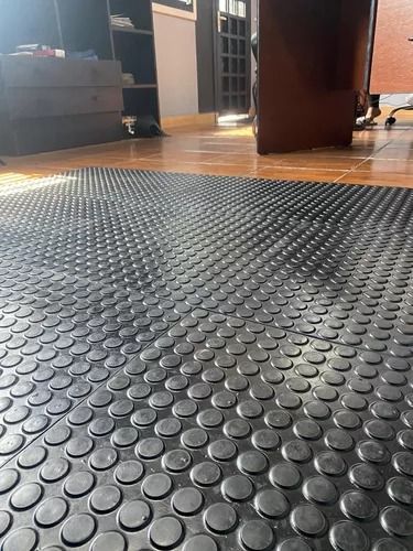 Alfombra de goma negra con protuberancias circulares sobre un piso de madera.