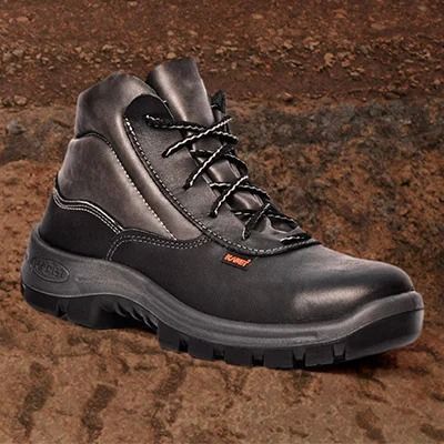 Bota de trabajo negra sobre una superficie rocosa y marrón. Tiene cordones y suela gruesa.